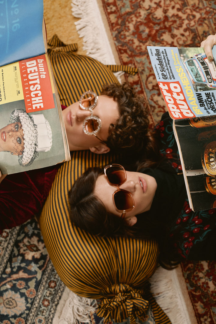 Eine junge Frau und ein junger Mann liegen auf dem Rücken und tragen Vintage-Sonnenbrillen